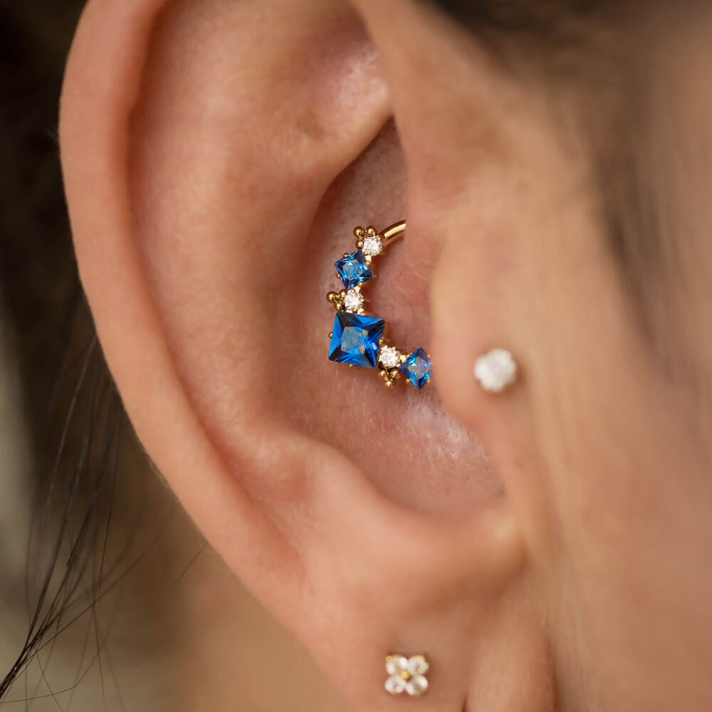 Złoty kolczyk do piercingu daith z niebieskimi cyrkoniami klasy 5A i białymi akcentami – elegancka, hipoalergiczna biżuteria do ucha w stylizacji premium od Body Blink Sopot.